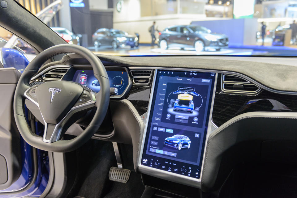 BRUSSELS, Belgium - January 13, 2017: Luxurious interior design of the Tesla Model X 90D luxury electric SUV SUV with large touchscreen display and dashboard.  The car has leather seats and aluminum details.  The Model X uses falcon wing doors to access the second and third row seats.  The car is displayed on the car display, with the lights off the body.  There are people looking around and other cars displayed in the background.